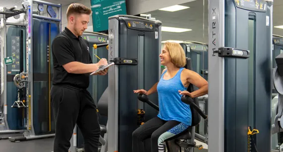 Wellness coach with clipboard with member on machine 