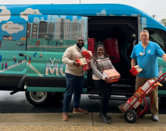 three staff members standing infront of a van with donated food items